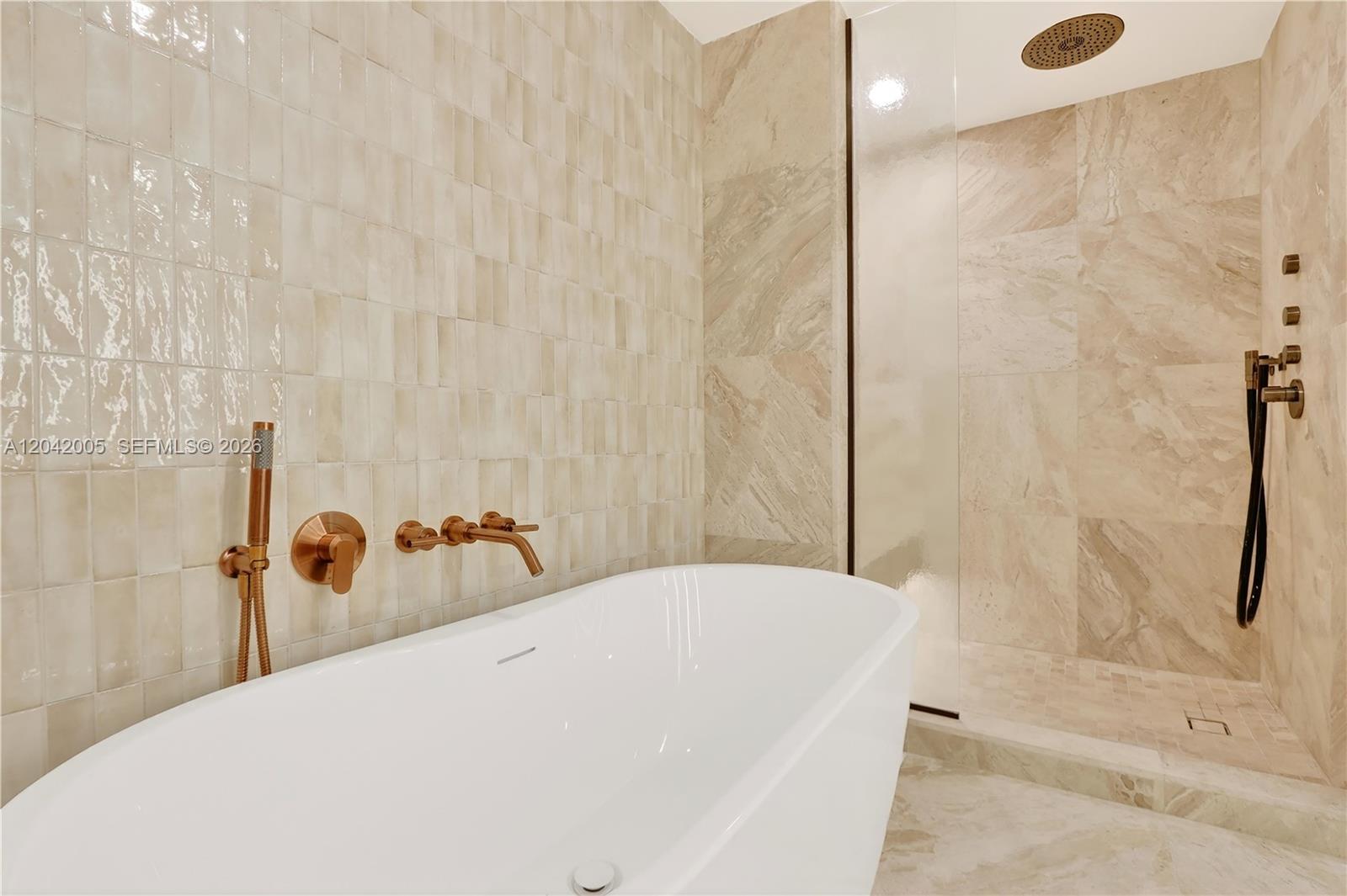 A modern bathroom features a white freestanding tub, a glass-enclosed shower, and bronze fixtures — 1176 97th St # 703, Bay Harbor Islands FL 33154, BAY HARBOR ISLANDS, FL