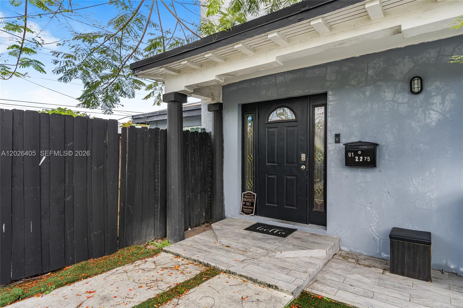 The exterior view shows a grey house entrance with a black door and wooden fence — 2275 NW 30th St, Miami FL 33142, MIAMI, FL