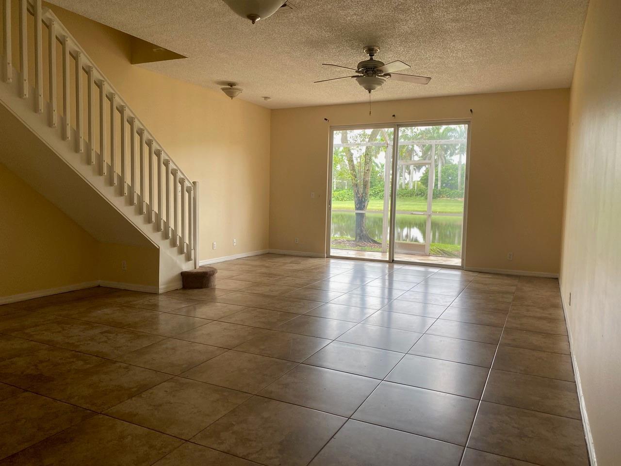 An empty living room with tile flooring, a staircase, and sliding glass doors overlooking a lake — 2253 Salerno Circle # 2253, Weston FL 33327, WESTON, FL