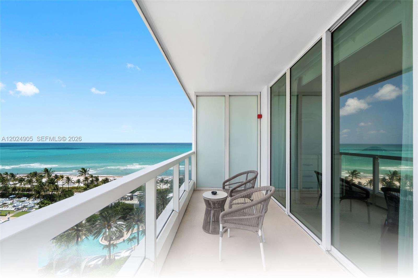 A balcony with two chairs and a small table overlooks the ocean and pool — 4391 Collins Ave # 1001, Miami Beach FL 33140, MIAMI BEACH, FL