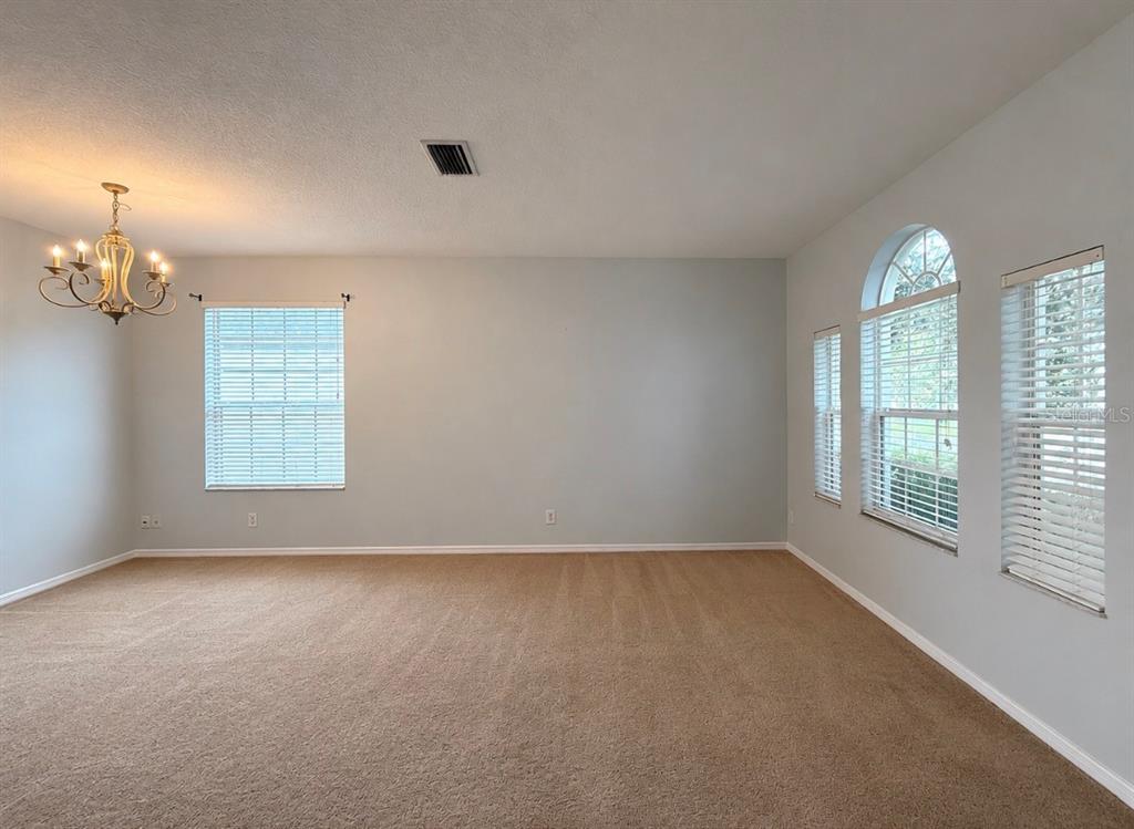 An empty room with beige carpet, light gray walls, a chandelier, and several windows — 9630 BATON ROUGE LANE, LAND O LAKES, FL