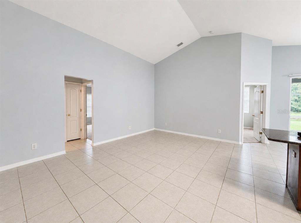 An empty room with light gray walls, vaulted ceilings, and large beige floor tiles — 9630 BATON ROUGE LANE, LAND O LAKES, FL