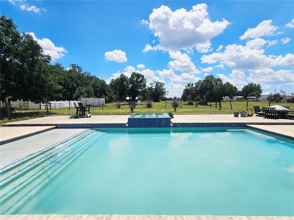A swimming pool with an attached spa sits on a patio overlooking a grassy field — 2445 SE AIRPORT ESTATES STREET, ARCADIA, FL
