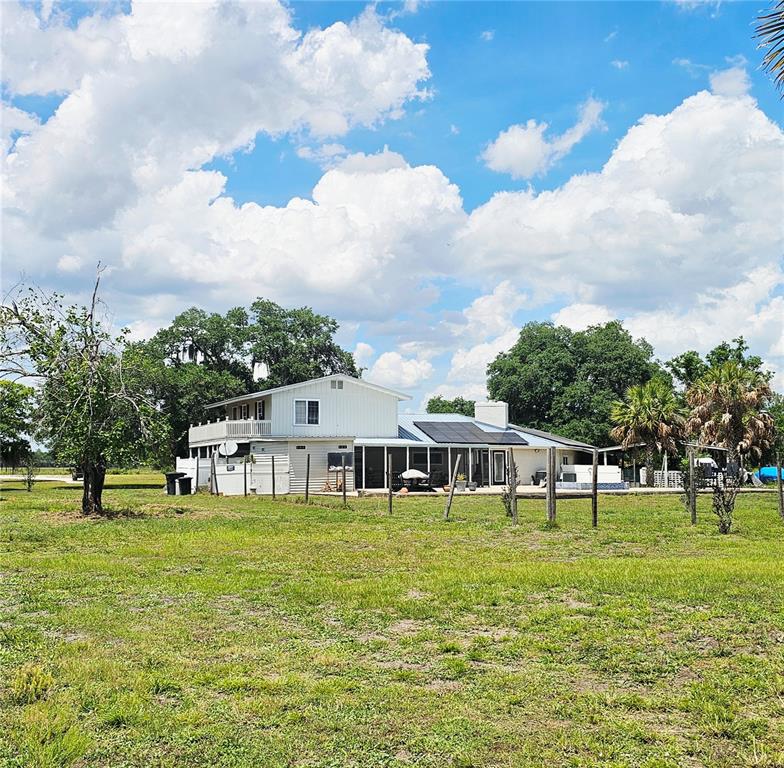 A two-story house with solar panels on the roof sits in a grassy field — 2445 SE AIRPORT ESTATES STREET, ARCADIA, FL