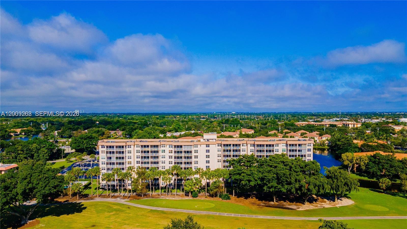 An aerial view shows a multi-story apartment building surrounded by trees, grass, and water — 250 Jacaranda Dr # 508, Plantation FL 33324, PLANTATION, FL