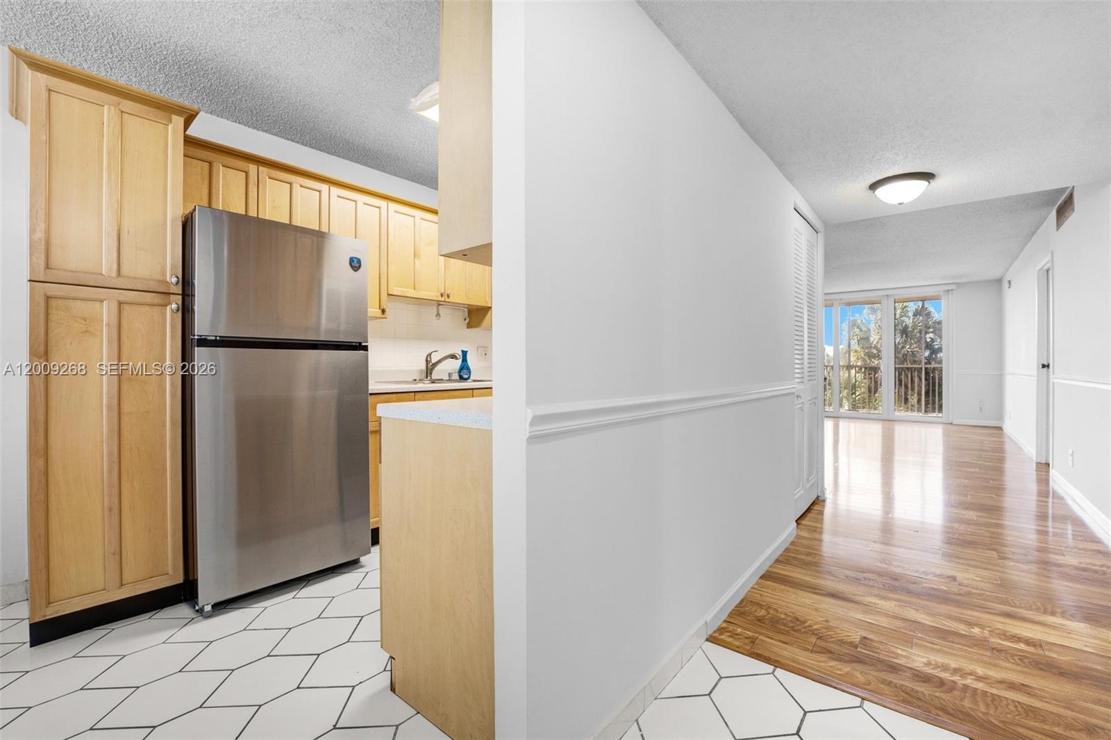 A kitchen with light wood cabinets and a stainless steel refrigerator opens to a hallway — 250 Jacaranda Dr # 508, Plantation FL 33324, PLANTATION, FL