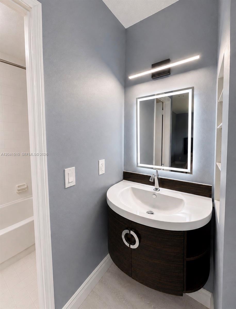 A bathroom features a curved dark wood vanity, a backlit mirror, and a wall-mounted light — 1120 NE 209th Ter, Miami FL 33179, MIAMI, FL