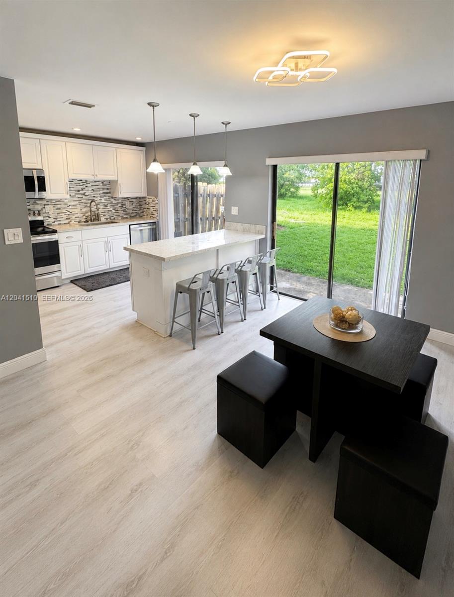 A kitchen with white cabinets and a center island opens to a dining area — 1120 NE 209th Ter, Miami FL 33179, MIAMI, FL