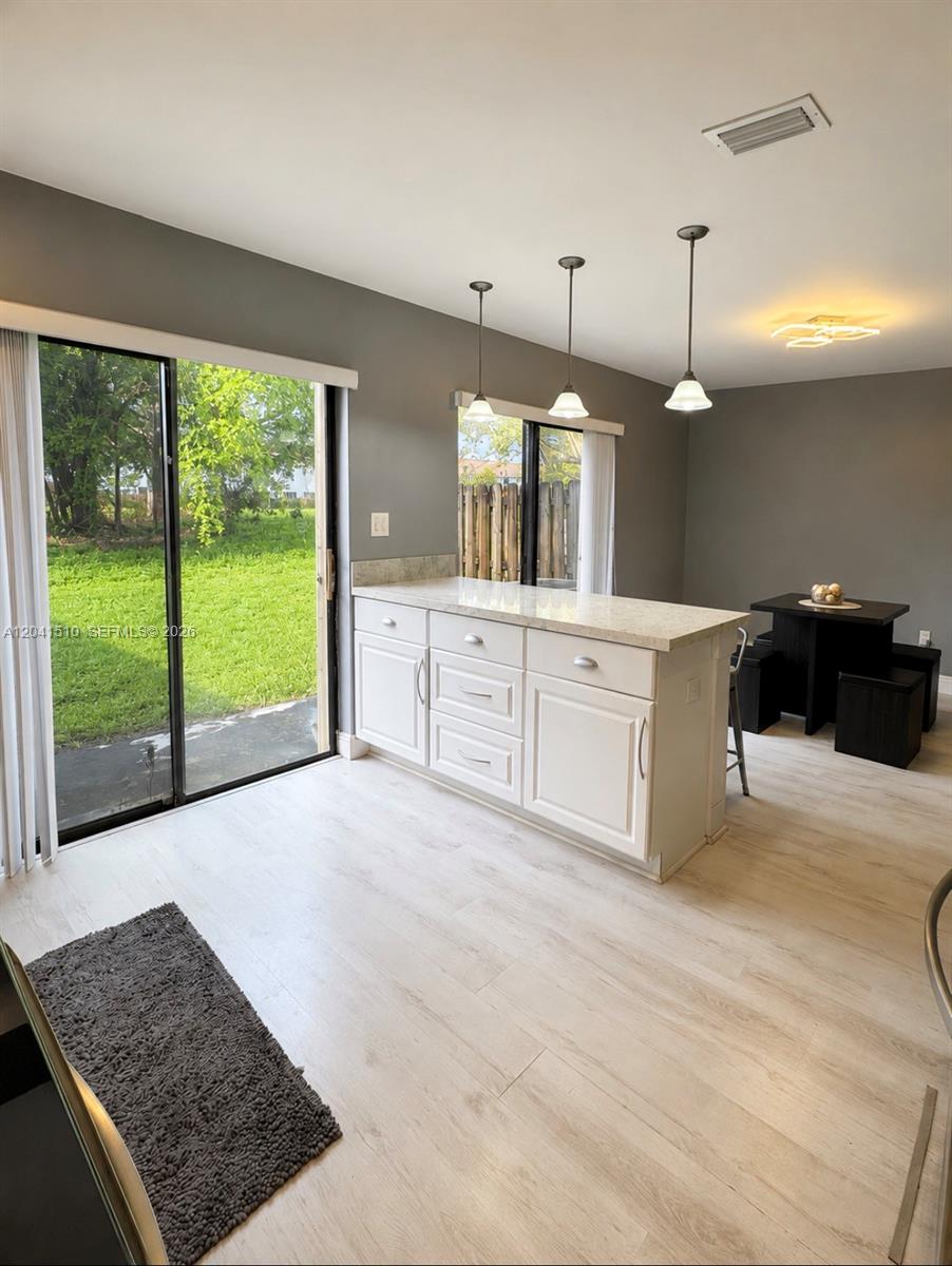 A kitchen island with white cabinets and a light countertop sits before a sliding glass door — 1120 NE 209th Ter, Miami FL 33179, MIAMI, FL