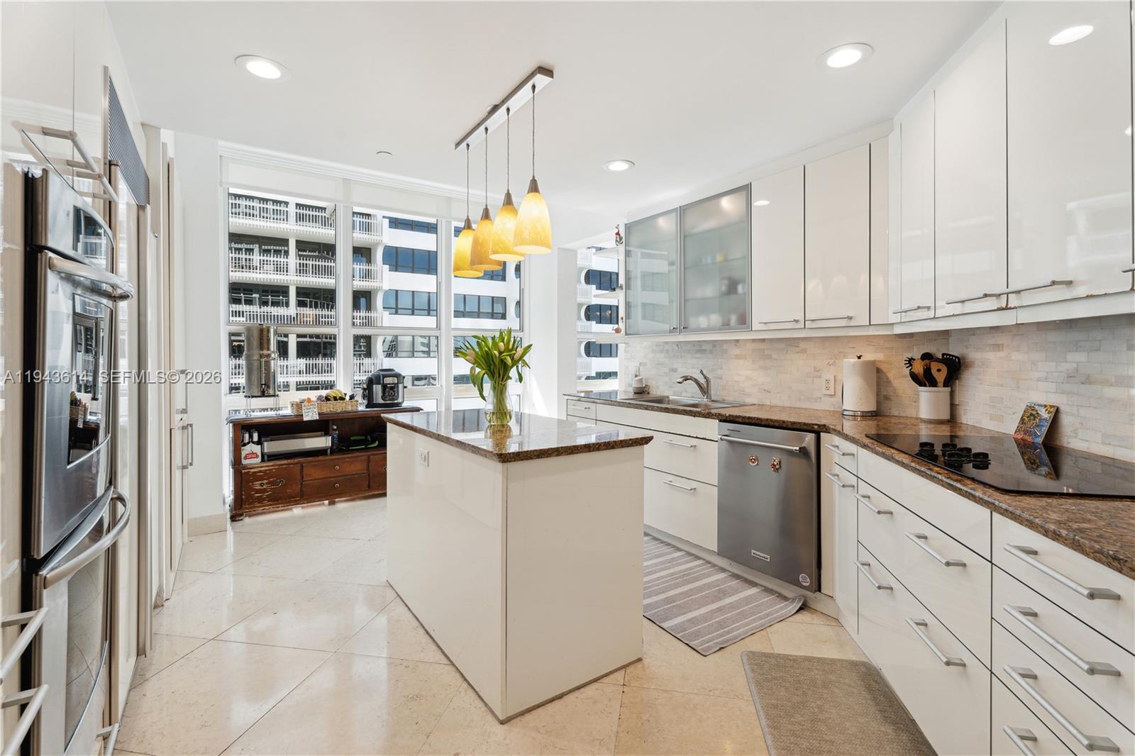 A modern kitchen features white cabinets, granite countertops, a central island, and floor-to-ceiling windows — 10225 Collins Ave # 904, Bal Harbour FL 33154, BAL HARBOUR, FL
