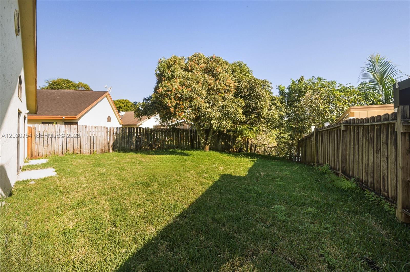 A grassy backyard features a wooden fence, a large tree, and a house exterior — NORTH LAUDERDALE, FL