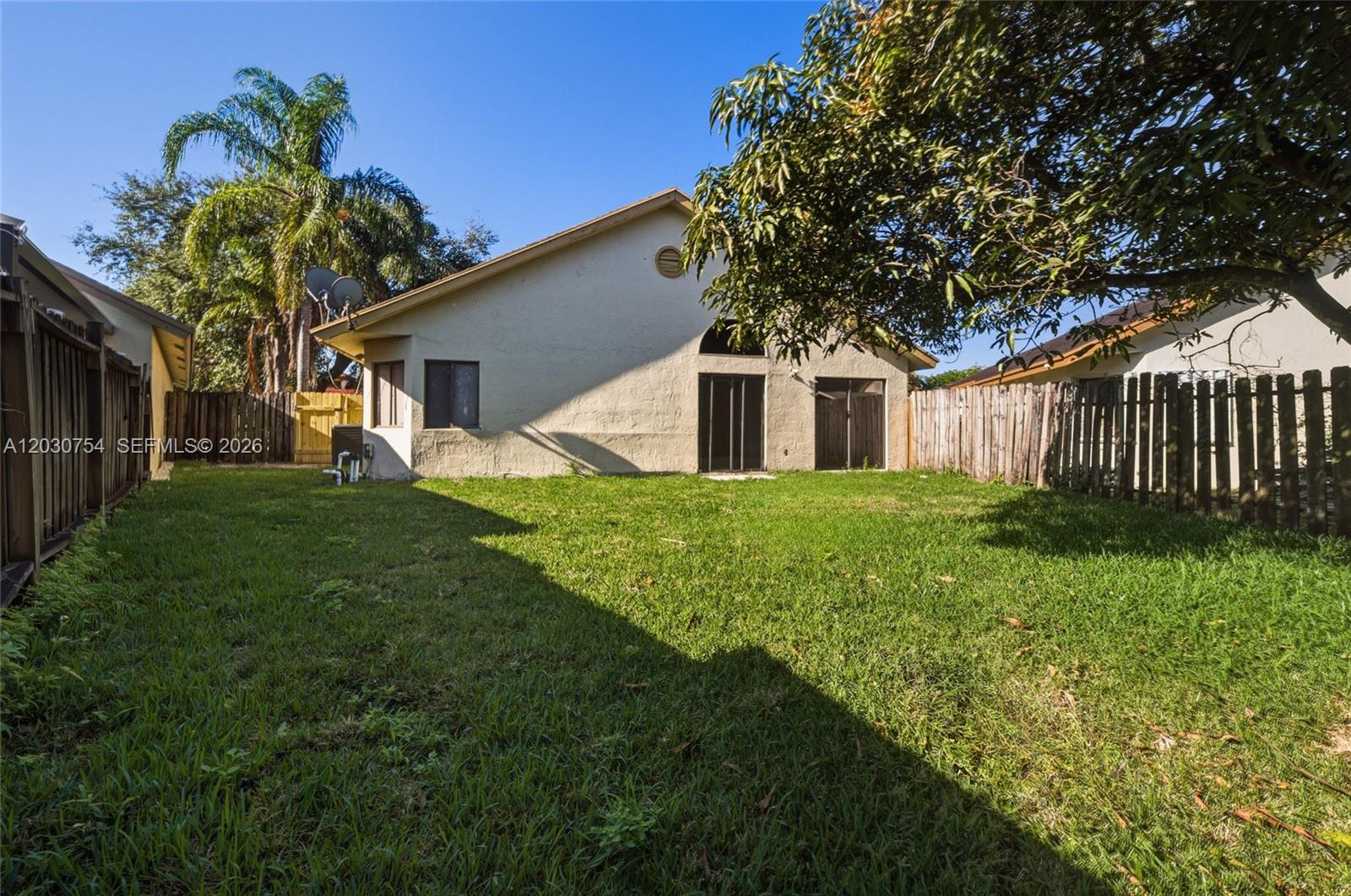 The backyard features a grassy lawn, a wooden fence, and the rear exterior of a house — NORTH LAUDERDALE, FL