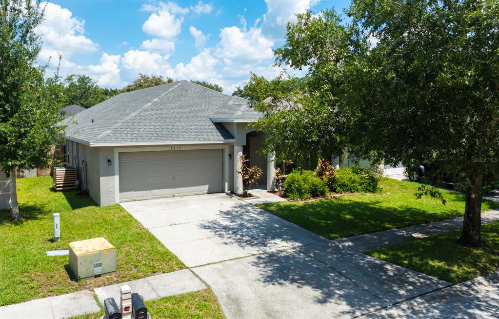An exterior view of a single-story house with a gray roof and a concrete driveway — 4517 WILD PLUM LANE, LUTZ, FL