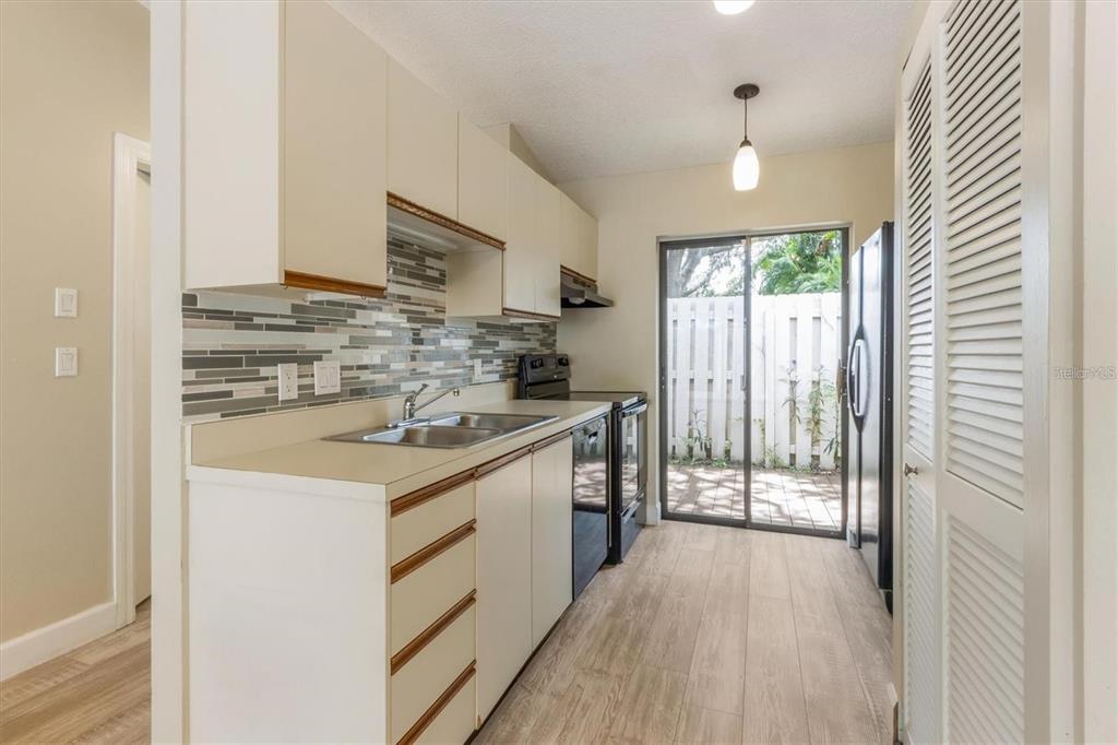 A kitchen features white cabinets, a tiled backsplash, stainless steel appliances, and a sliding door — 2903 62ND STREET W UNIT 303, BRADENTON, FL