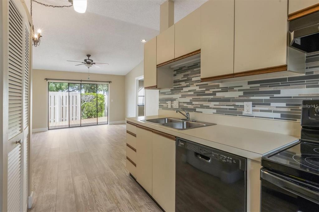 A kitchen with light-colored cabinets and a mosaic backsplash overlooks a living area with flooring — 2903 62ND STREET W UNIT 303, BRADENTON, FL