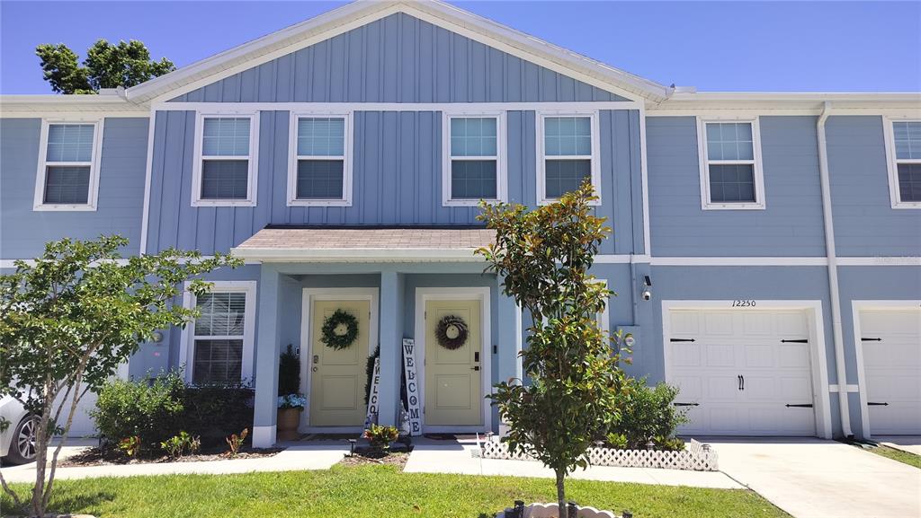 A two-story blue townhouse with light-colored doors and attached garages under a clear sky — 12250 GRIZZLY LANE, NEW PORT RICHEY, FL