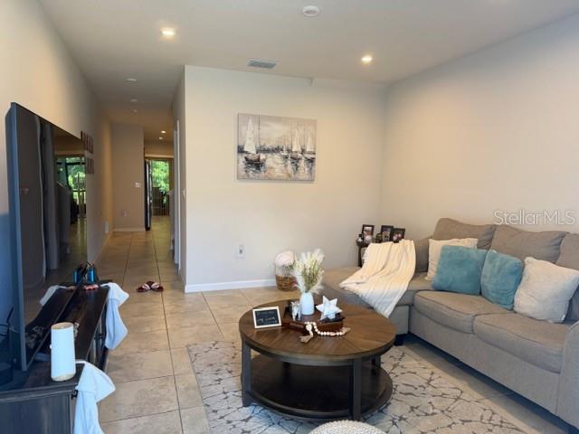 A living room features a sectional sofa, a round coffee table, and tile flooring — 12250 GRIZZLY LANE, NEW PORT RICHEY, FL