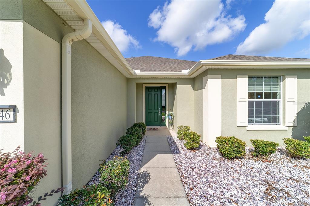 A concrete walkway leads to the green front door of a light-colored stucco house — 7346 SW 101ST COURT, OCALA, FL