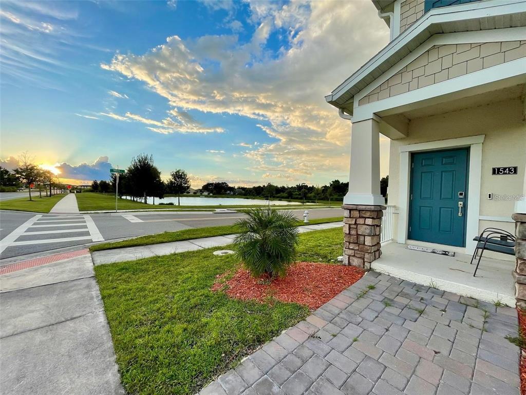 A teal front door with a stone-accented porch overlooks a street and a small pond — 1543 CROSS PRAIRIE PARKWAY, KISSIMMEE, FL