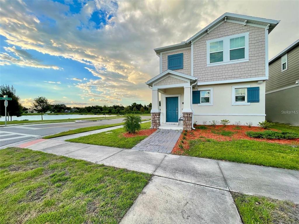 A two-story house with a blue door, stone accents, and a paved walkway near water — 1543 CROSS PRAIRIE PARKWAY, KISSIMMEE, FL