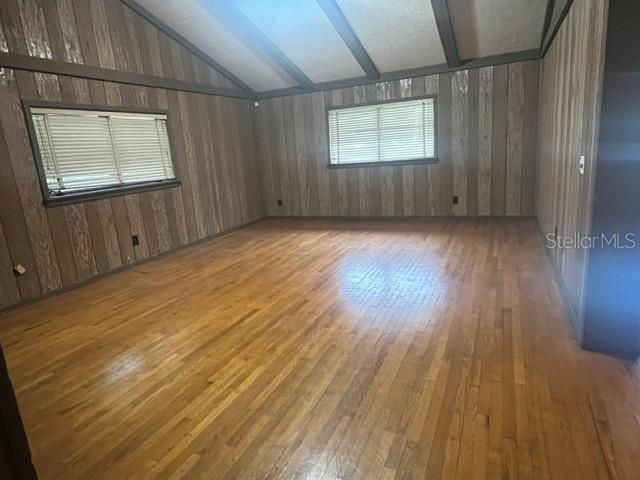 An empty room features wood-paneled walls, hardwood floors, and a vaulted ceiling with exposed beams — 1825 N DEAN ROAD, ORLANDO, FL