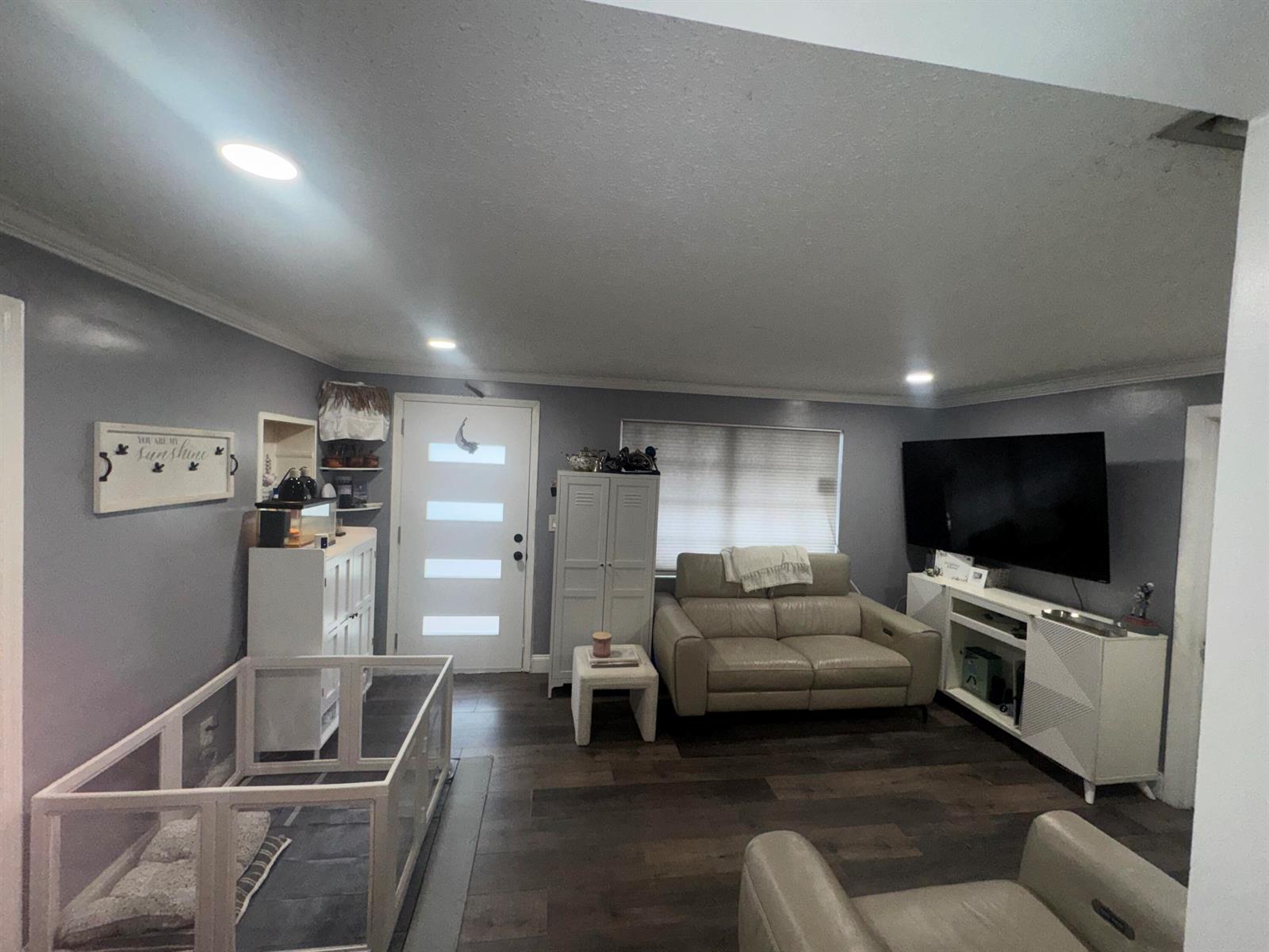 A living room features gray walls, dark wood flooring, a white front door, and a pet pen — 4328 Pine Street, FL 33406, FL