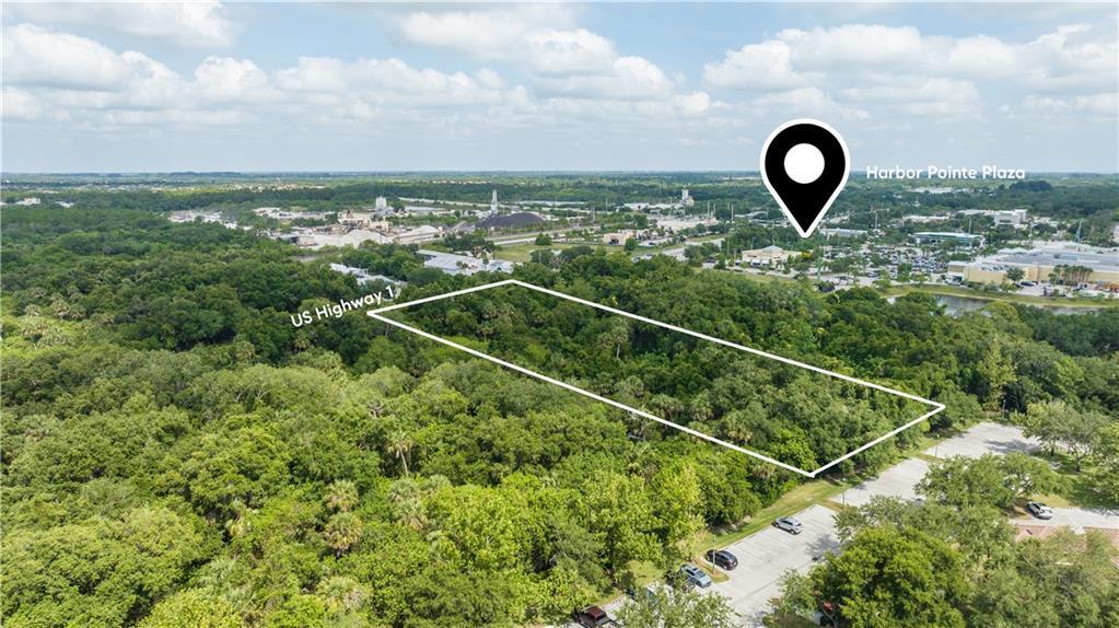 An aerial view shows a rectangular plot of undeveloped land near a shopping plaza — VERO BEACH, FL