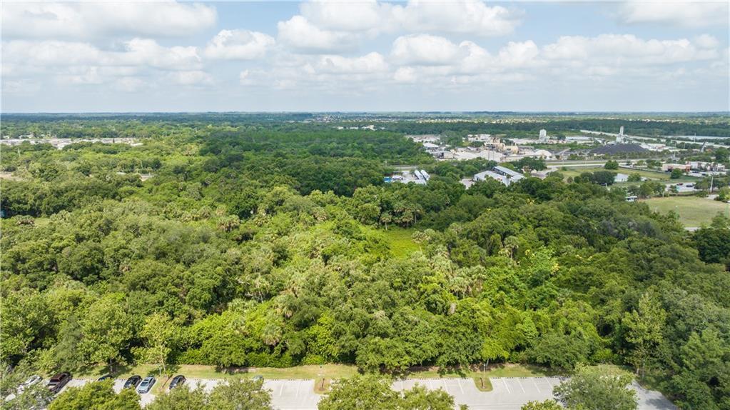 An aerial view shows a large, dense wooded area adjacent to a paved parking lot — VERO BEACH, FL