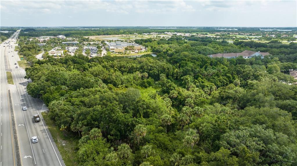 An aerial view shows a wooded lot adjacent to a highway and commercial buildings — VERO BEACH, FL