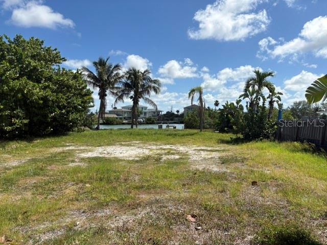 A vacant, grassy waterfront lot features palm trees and a view of distant houses — 14065 N BAYSHORE DRIVE, MADEIRA BEACH, FL