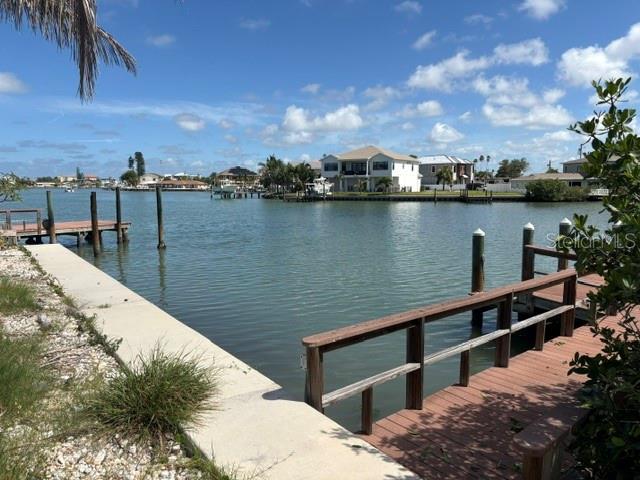 A wooden dock extends into a calm canal with houses visible on the opposite shore — 14065 N BAYSHORE DRIVE, MADEIRA BEACH, FL