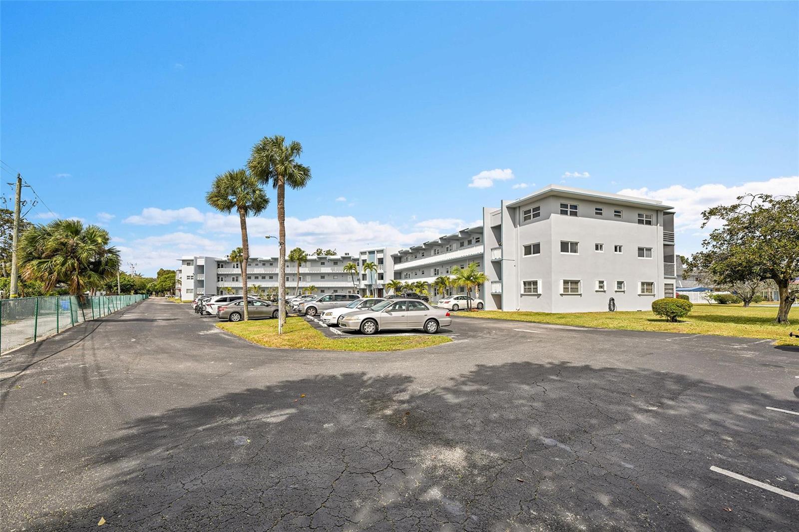 A multi-story apartment building with a parking lot and palm trees under a blue sky — 2223 Park Lane # 302, Hollywood FL 33021, HOLLYWOOD, FL