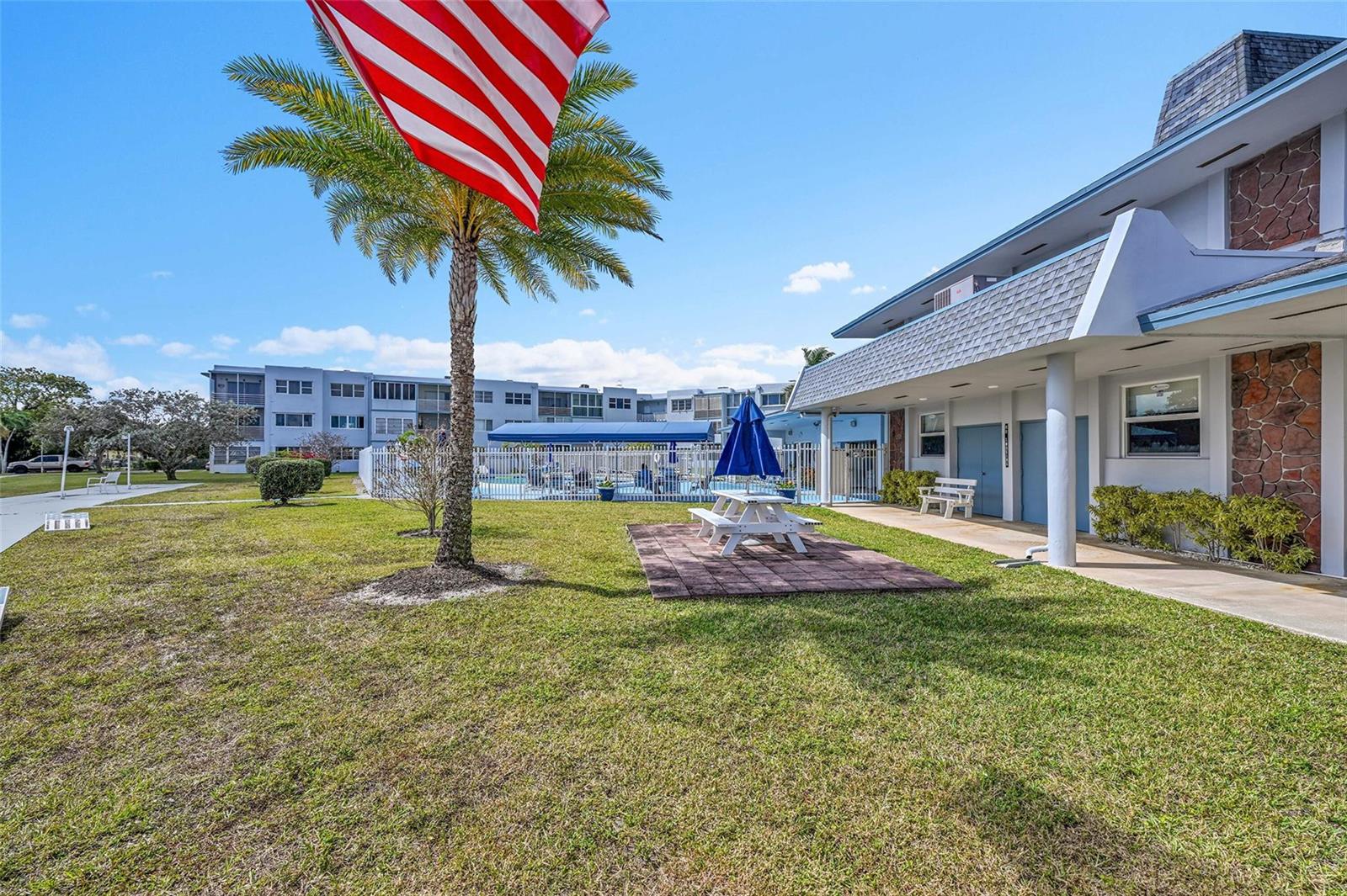 A grassy courtyard features a palm tree, a picnic table with an umbrella, and buildings — 2223 Park Lane # 302, Hollywood FL 33021, HOLLYWOOD, FL