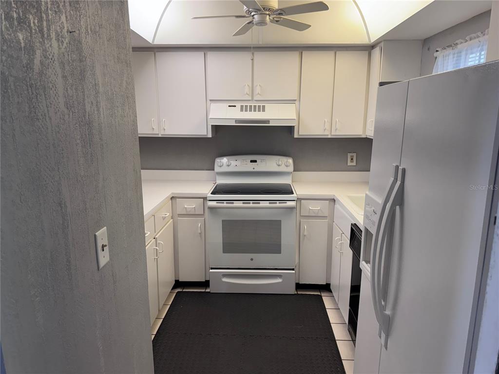 A kitchen features white cabinets, white appliances, a ceiling fan, and a black floor mat — 1201 N MCMULLEN BOOTH ROAD, CLEARWATER, FL