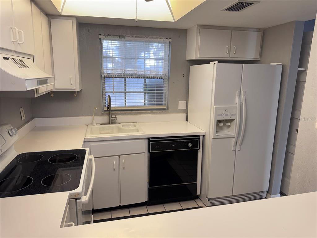 A kitchen features white cabinets, a black dishwasher, a white refrigerator, and a window — 1201 N MCMULLEN BOOTH ROAD, CLEARWATER, FL