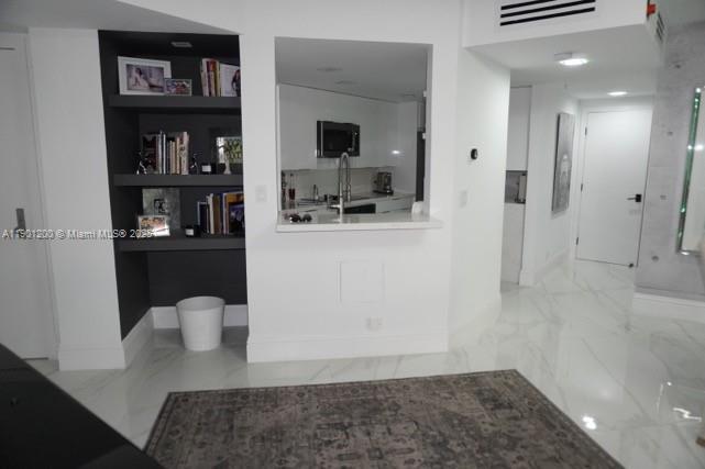 A kitchen pass-through window overlooks a room with dark built-in shelving and white marble floors — 701 Brickell Key Blvd # 412, Miami FL 33131, MIAMI, FL