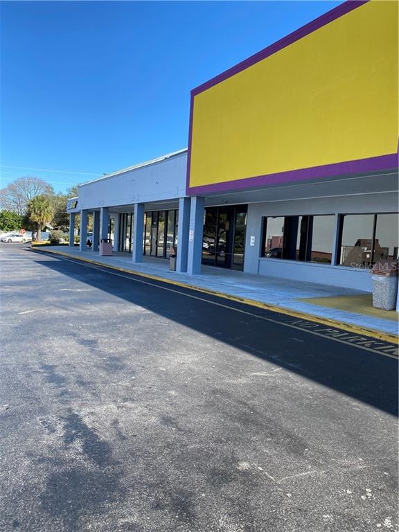 A commercial building exterior features a large yellow sign above a glass storefront and sidewalk — 1861 N HIGHLAND AVENUE, CLEARWATER, FL