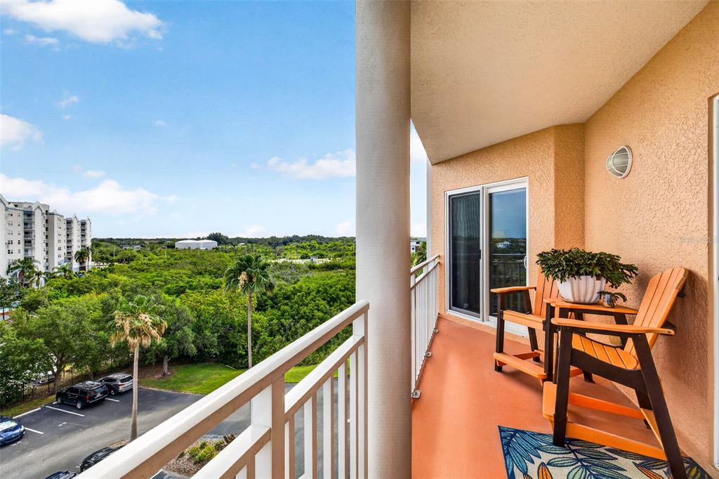 A balcony with two wooden chairs overlooks a parking lot and a dense green forest — 4516 SEAGULL DRIVE UNIT 615, NEW PORT RICHEY, FL