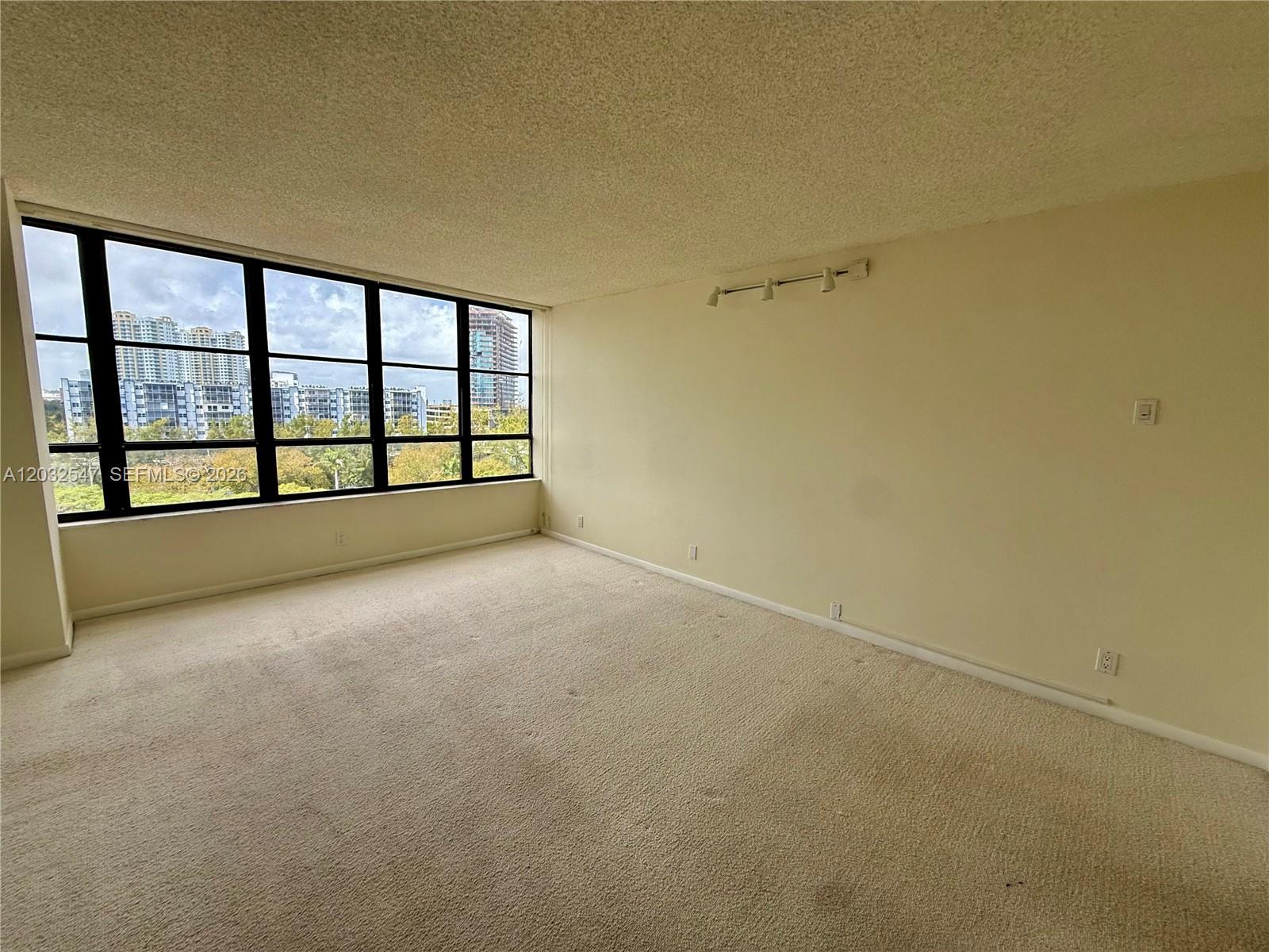 An empty room features beige carpeting, light-colored walls, and a large window with city views — 500 Three Islands Blvd # 314, Hallandale Beach FL 33009, HALLANDALE BEACH, FL