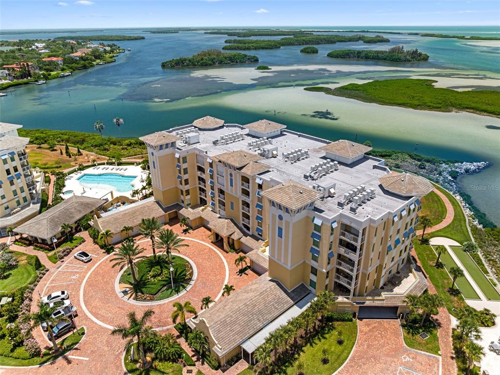 An aerial view shows a multi-story yellow building with a circular driveway and swimming pool — 795 COLLANY ROAD UNIT 204, TIERRA VERDE, FL