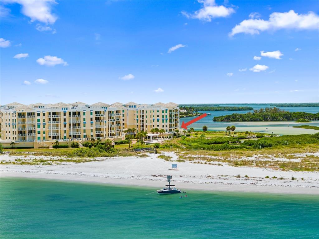 An aerial view shows a large beachfront apartment complex with a boat anchored nearby — 795 COLLANY ROAD UNIT 204, TIERRA VERDE, FL