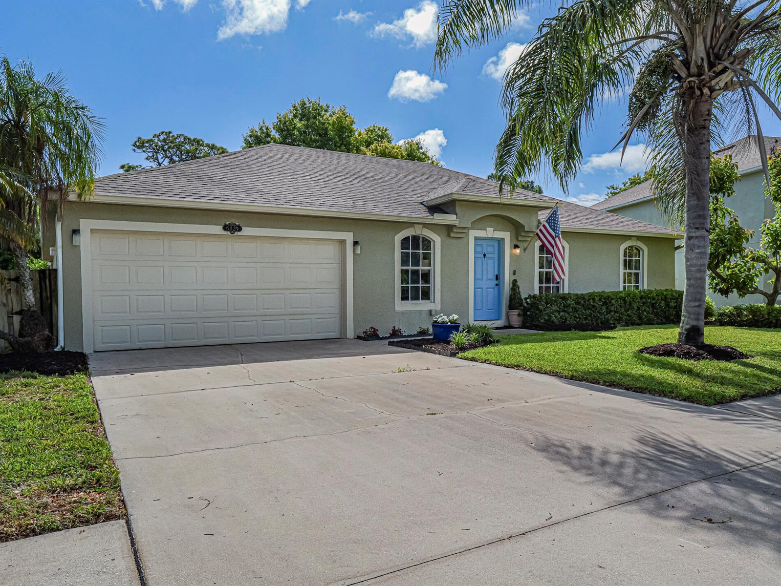 A single-story house with a light green exterior, a blue front door, and a concrete driveway — 6029 Ridge Lake Circle, Vero Beach FL 32967, VERO BEACH, FL