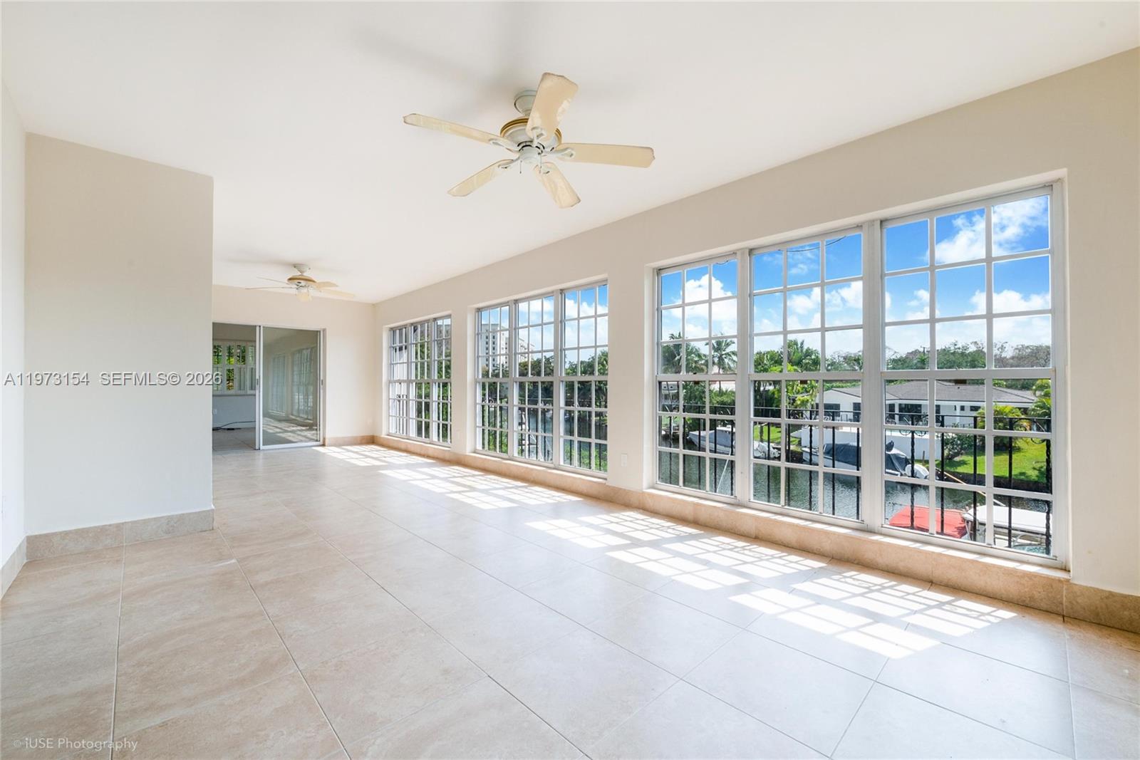 A sunroom with tile flooring, ceiling fans, and large windows overlooking a canal — 1265 S Alhambra Cir # B, Coral Gables FL 33146, CORAL GABLES, FL