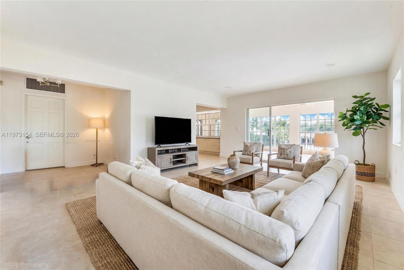 A bright living room features a large sectional sofa, a television, and sliding glass doors — 1265 S Alhambra Cir # B, Coral Gables FL 33146, CORAL GABLES, FL