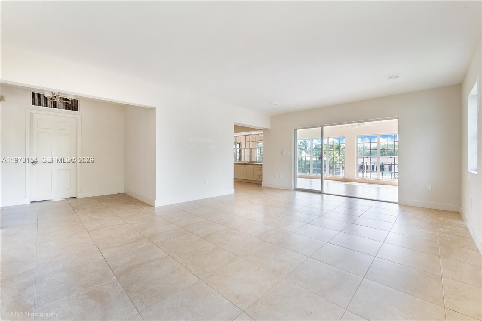 An empty living room features light tile flooring, white walls, and a sliding glass door — 1265 S Alhambra Cir # B, Coral Gables FL 33146, CORAL GABLES, FL