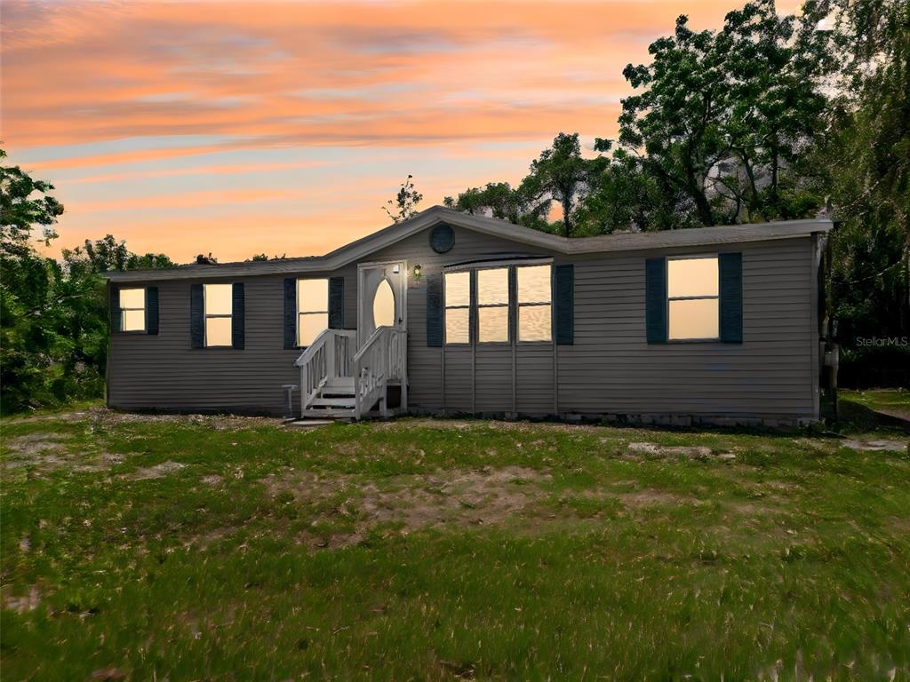 A single-story manufactured home with grey siding and a small wooden porch at sunset — 1819 SINCLAIR HILLS ROAD, LUTZ, FL