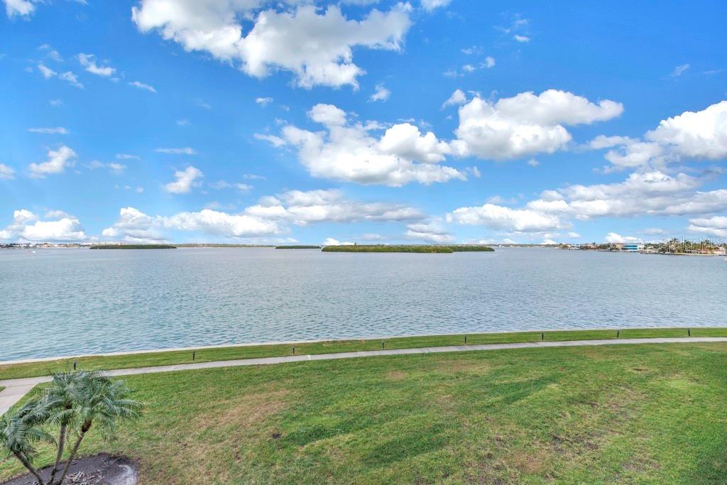 A grassy lawn overlooks a wide bay with distant islands under a blue, cloudy sky — 1 KEY CAPRI UNIT 209E, TREASURE ISLAND, FL