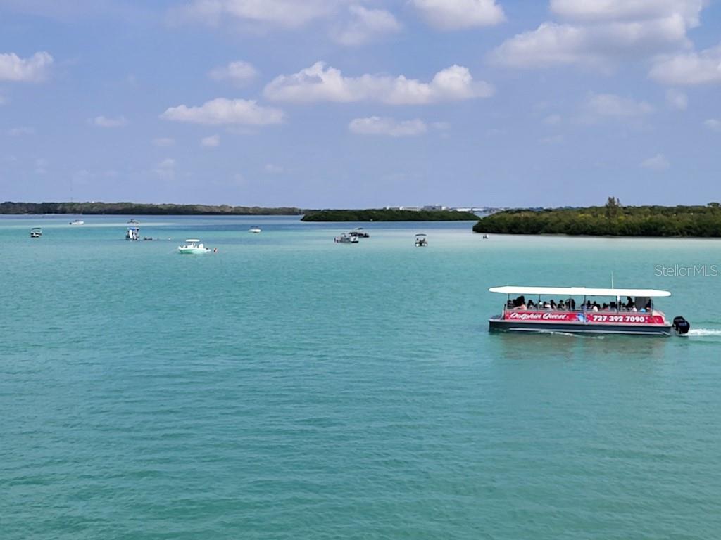A tour boat travels through turquoise water near mangrove islands under a blue sky — 1 KEY CAPRI UNIT 209E, TREASURE ISLAND, FL