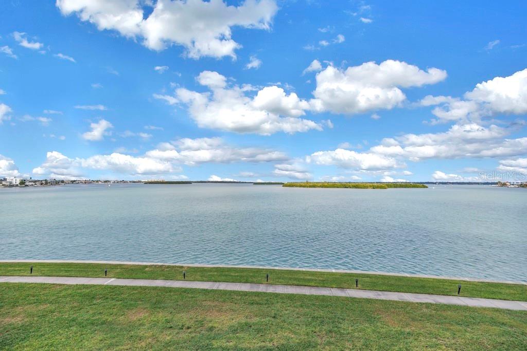 A grassy lawn borders a concrete walkway overlooking a large bay with distant islands — 1 KEY CAPRI UNIT 209E, TREASURE ISLAND, FL