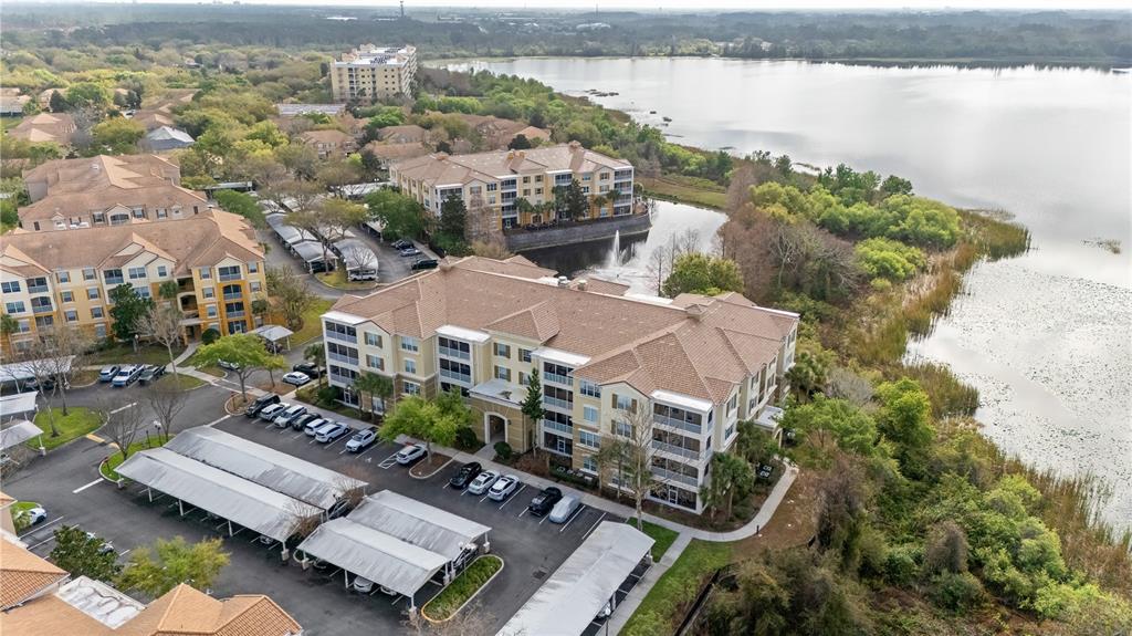 An aerial view shows multi-story apartment buildings with parking carports situated beside a large lake — 3362 ROBERT TRENT JONES DRIVE UNIT 10407, ORLANDO, FL